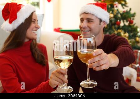 Coppia che indossa il cappello di santa guardando l'un l'altro sorridendo e. tostatura mentre si è seduti in soggiorno Foto Stock