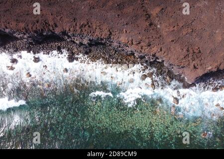 Vista aerea dall'alto delle onde che spruzzano sulla costa vulcanica rocciosa. Foto di alta qualità Foto Stock