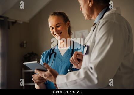 Due medici sorridono mentre discutono i risultati del paziente su un tablet digitale. Foto Stock