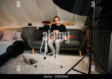 Musicista maschio caucasico che suona canzoni e registra musica in camera da letto studio Foto Stock