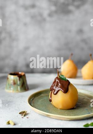 dessert con pera d'oro in camicia, cioccolato fuso versato. sfondo grigio. Foto Stock