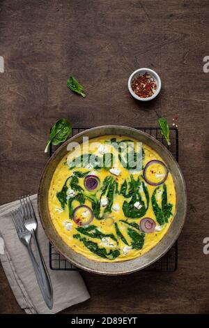 frittata o omelette deliziose fatte in casa con spinaci, formaggio feta, cipolle rosse in una padella di ferro su un tavolo rustico. Vista dall'alto Foto Stock