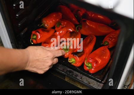 Persona che controlla sulla torrefazione dei peperoni rossi nel forno Foto Stock