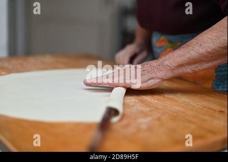 Primo piano delle mani di una donna anziana che rotola fuori l'impasto un tagliere Foto Stock