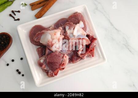 Carni fresche di capra cruda o pezzi di montone o di agnello. Preparazione per il curry di montone indiano. Spezie sullo sfondo come bastoncini di cannella, peperoncino rosso in polvere, Foto Stock