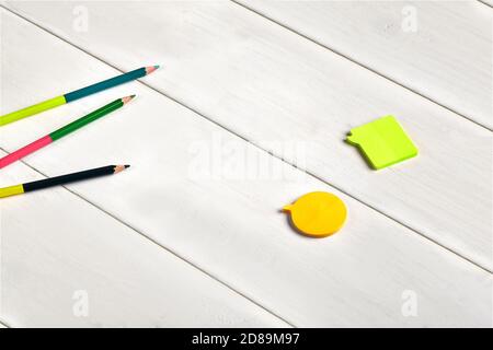 Matite colorate su due lati, note appiccicose arancioni e gialle su scrivania o sfondo di legno bianco. Primo piano, spazio di copia, vista dall'alto Foto Stock