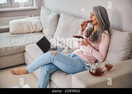 Donna affascinante che mangia deliziosi biscotti a casa Foto Stock