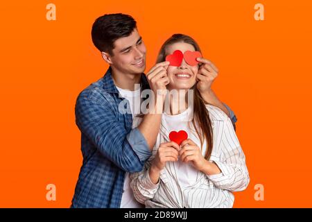 Felice ragazzo giovane in casual guarda la donna e mette cuori rossi sui suoi occhi sulla data romantica Foto Stock