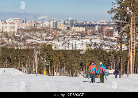 Ekaterinburg, Russia - 26 febbraio 2019. Una coppia in tute e con snowboard cammina fino alla cima della pista di allenamento del complesso sportivo su M. Foto Stock