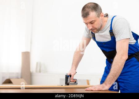 Tappeto professionale che lavora usando la pistola di graffetta che fa la mobilia che si trova in piedi all'interno Foto Stock