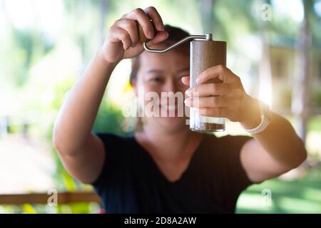 Una donna asiatica che macina il caffè con un macinacaffè a mano. Foto Stock
