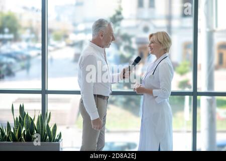 Donna bionda dottore che parla al microfono, rispondendo alle domande dei giornalisti maschili Foto Stock