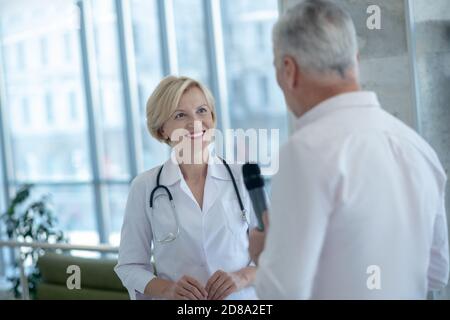 Giornalista di sesso maschile con capelli grigi che ha intervistato una donna blonde sorridente dottoressa Foto Stock