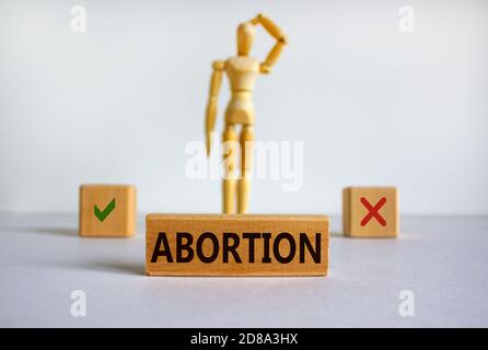 Parola 'aborto' scritta in blocco di legno. Modello in legno di un uomo che riflette su una scelta. Splendido sfondo bianco, spazio per la copia. Concetto. Foto Stock