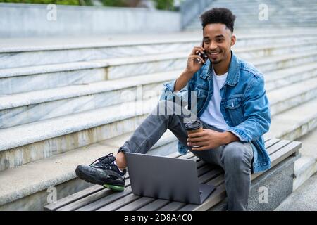 Sorridente giovani freelancer parla al telefono sul banco di lavoro con computer portatile Foto Stock