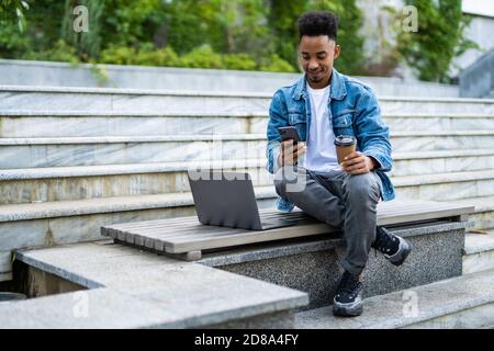 Sorridente giovani freelancer parla al telefono sul banco di lavoro con computer portatile Foto Stock