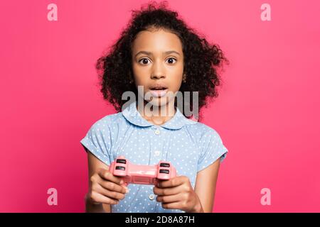 KYIV, UCRAINA - 9 GIUGNO 2020: Scioccato carino curly africano americano capretto con joystick isolato su rosa Foto Stock