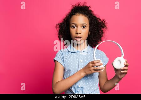 scioccato carino ricciolo afroamericano con le cuffie isolate rosa Foto Stock