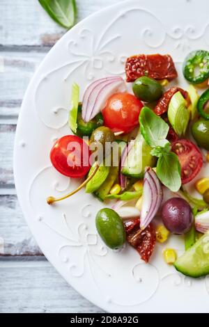 Insalata semplice con olive verdi e Kalamata, cetrioli, ciliegi e pomodori marinati, capperi e peperoni Jalapeno. Luminoso sfondo in legno. Foto Stock