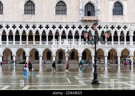 Acque alte - acqua alta causa inondazioni in Piazza San Marco. Un lampione veneziano tradizionale e turisti che guado attraverso l'acqua in wellingtons. Venezia Foto Stock