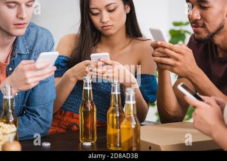 concentrazione selettiva di amici multietnici che chiacchierano sugli smartphone vicino alla birra durante la festa Foto Stock