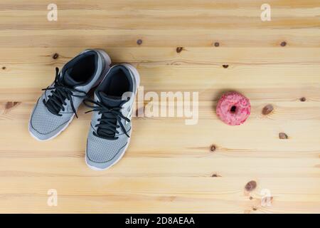 Sneaker grigie, scarpe sportive da running da donna e ciambella rosa alla fragola sul lato. Decisione di stile di vita sano, mangiare sano vs. Processato fo Foto Stock