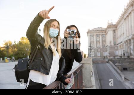 Alcune ragazze che cercano e fotografano una parte della città. Entrambi indossano maschere facciali. Concetto di turismo e nuova normalità. Foto Stock