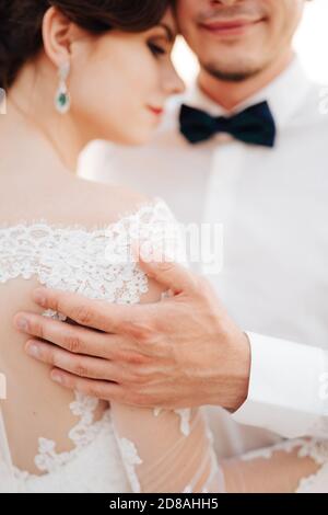 lo sposo abbraccia delicatamente la sposa con la mano la sua spalla Foto Stock