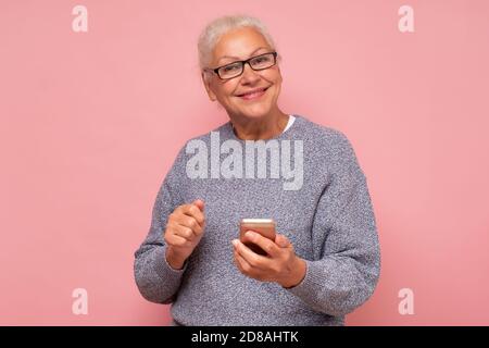 Donna con capelli grigi sorridenti matura con occhiali utilizzando smartphone e. sorridente Foto Stock