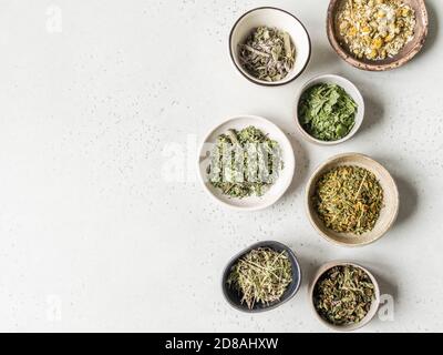 Varie erbe sane secche, fiori di piante per la preparazione di tè alle erbe in ciotole su sfondo grigio. Vista dall'alto. Spazio di copia Foto Stock