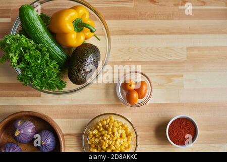 Vista ad alto angolo delle verdure fresche nel recipiente per l'insalata e altri ingredienti sulla tavola Foto Stock