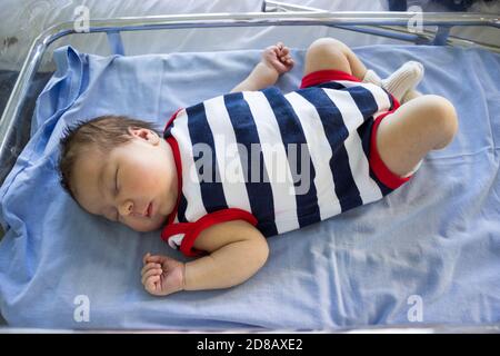 Il neonato dorme in un piccolo letto di vetro dell'ospedale, sdraiato sulla schiena in strip Foto Stock