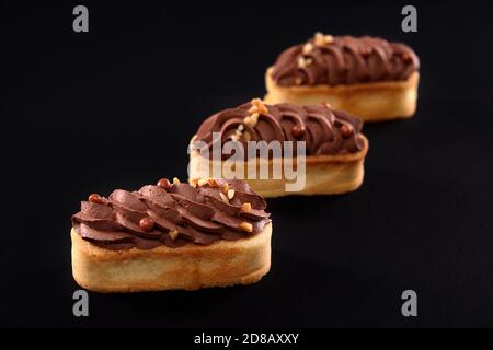 Biscotti frollini con mascarpone panna di cioccolato marrone montata sulla parte superiore. Tre dolci freschi fatti in casa isolati su sfondo nero. Concetto di dolci, dessert. Foto Stock