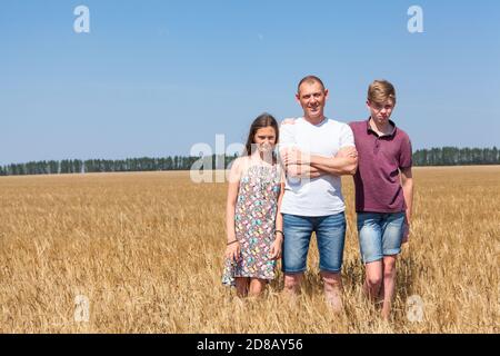 Papà con figlio e figlia pre-teen, ritratto a lunghezza intera, caucasico singolo padre con due bambini in piedi su campo di grano in estate, copyspace Foto Stock