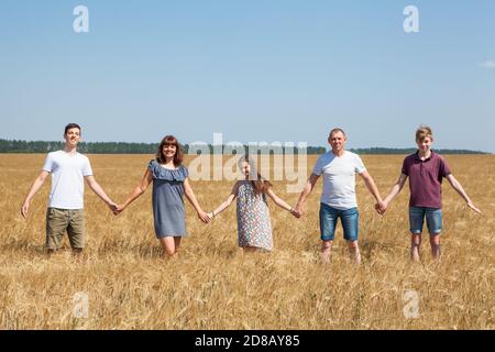 Grande famiglia di padre, madre, due fratelli e sorella che tengono le mani in linea sul campo di grano, ritratto a lunghezza intera Foto Stock