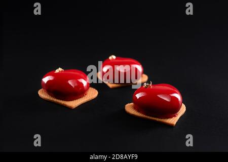 Torte rosse a cuore decorate con oro isolato su sfondo nero. Dessert con superficie liscia, mousse e glassa a specchio su biscotti dolci. Delizioso piatto in caffetteria. Foto Stock