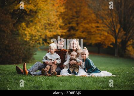 Bella famiglia seduta in un parco con autunno colorato alberi Foto Stock