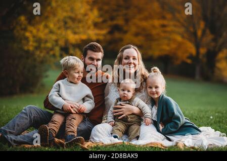 Bella famiglia seduta in un parco con autunno colorato alberi Foto Stock