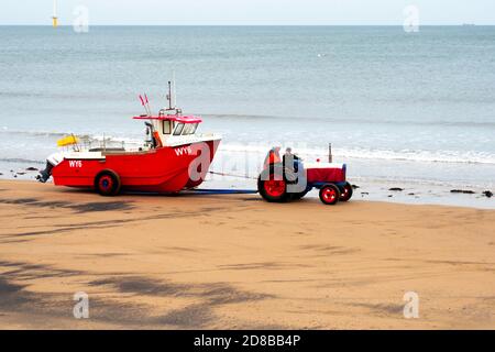 Pescatore che guida un trattore che trasporta la loro barca rossa WY6 Radiant Dawn out of the Sea Redcar Cleveland UK Foto Stock
