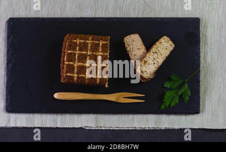Vista dall'alto di un pezzo di nutriente tempeh di soia tagliato a fette su un piatto d'ardesia con prezzemolo fresco e una forchetta di legno. Foto Stock