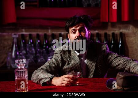 Uomo ubriaco seduto al bancone in un pub o in un bar e bere cognac o whiskey. Foto Stock