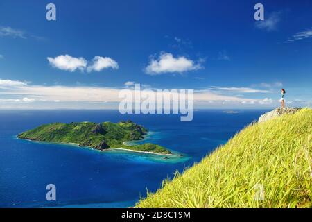 Vista di Kuata Island da Wayaseva Island con un escursionista in piedi su una roccia e Yasawa Islands, Isole Figi Foto Stock