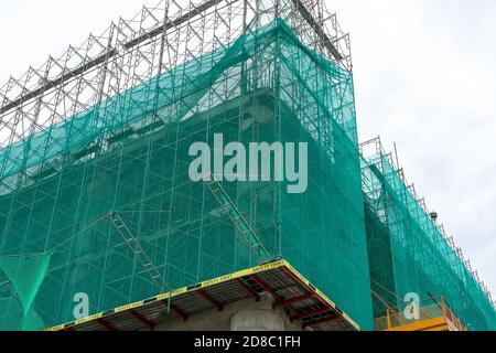 L'angolo della facciata dell'edificio in costruzione è coperto da una rete protettiva. Iscrizione sicurezza prima. Vista ad angolo basso. Foto Stock
