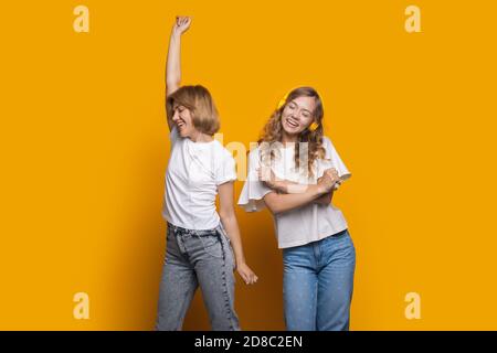 Bionda donna con il suo amico sta ascoltando musica sopra una parete gialla con cuffie e balli Foto Stock