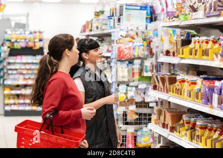 Un consulente di vendita in un supermercato aiuta il cliente nella scelta del prodotto. Vista laterale. Rifugi con cibi. Giovani donne di nazionalità caucasica. Foto Stock