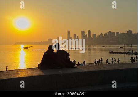 Una giovane coppia indiana guarda il tramonto sul Mar Arabico, mentre si siede sull'argine di Marine Drive, Mumbai, India Foto Stock