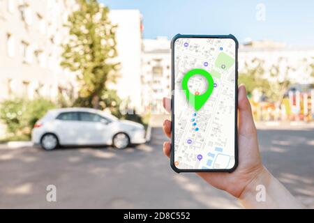 Una donna ha un cellulare con un'app mappa online, primo piano mano. Sullo sfondo è una strada cittadina con auto. Il concetto di navigazione online e mod Foto Stock