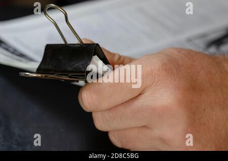 Primo piano delle mani maschili che tengono fogli di carta con clip in metallo nero. I fogli sono riempiti di testo. Tracce di inchiostro blu sul dito dell'uomo. Messa a fuoco selettiva. Foto Stock