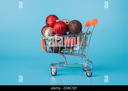 Primo piano foto profilo di piccolo metallo con ruote negozio carrello con pila di pallina giocattolo regalo presenta isolato sopra sfondo luminoso di colore blu Foto Stock