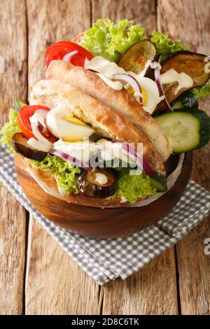 Panino Israeliano fast food sabich con verdure, uova e tahini primo piano sul tavolo. Verticale Foto Stock